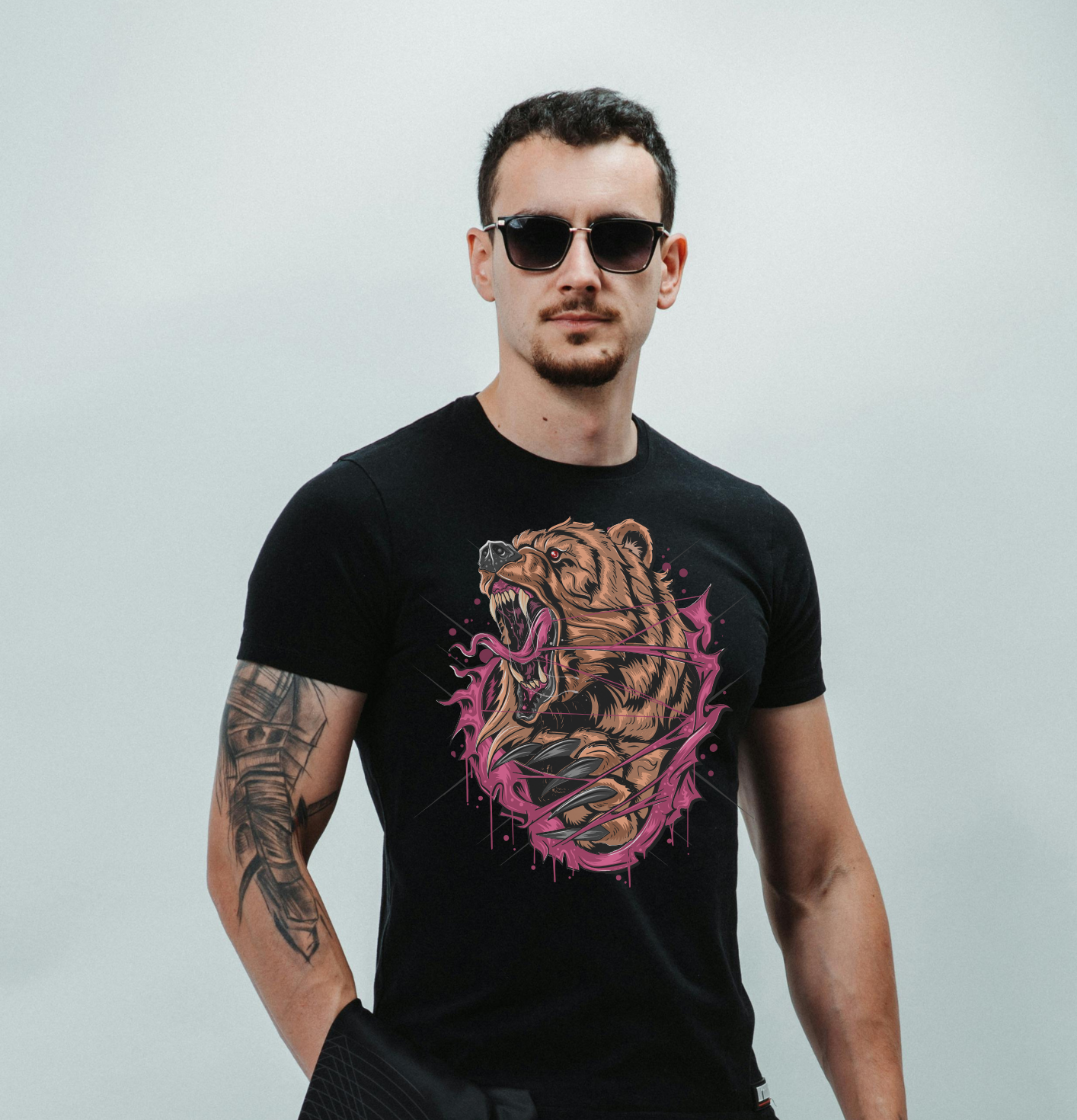 Man wearing a black t-shirt with a bear graphic design, sunglasses, and holding a jacket against a plain background.
